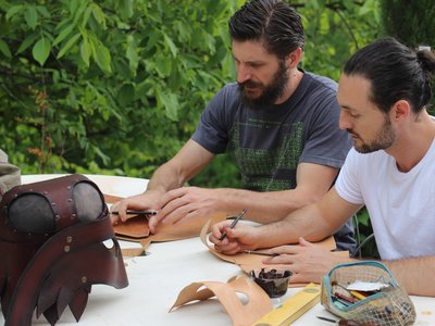 Deux membres de l'association travaillent le cuir pour en faire une pièce d'armure